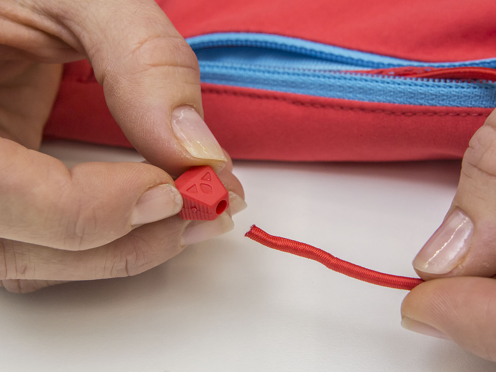 Eine Hand fädelt einen Kordelstopper auf den Gummizug einer Jacke auf