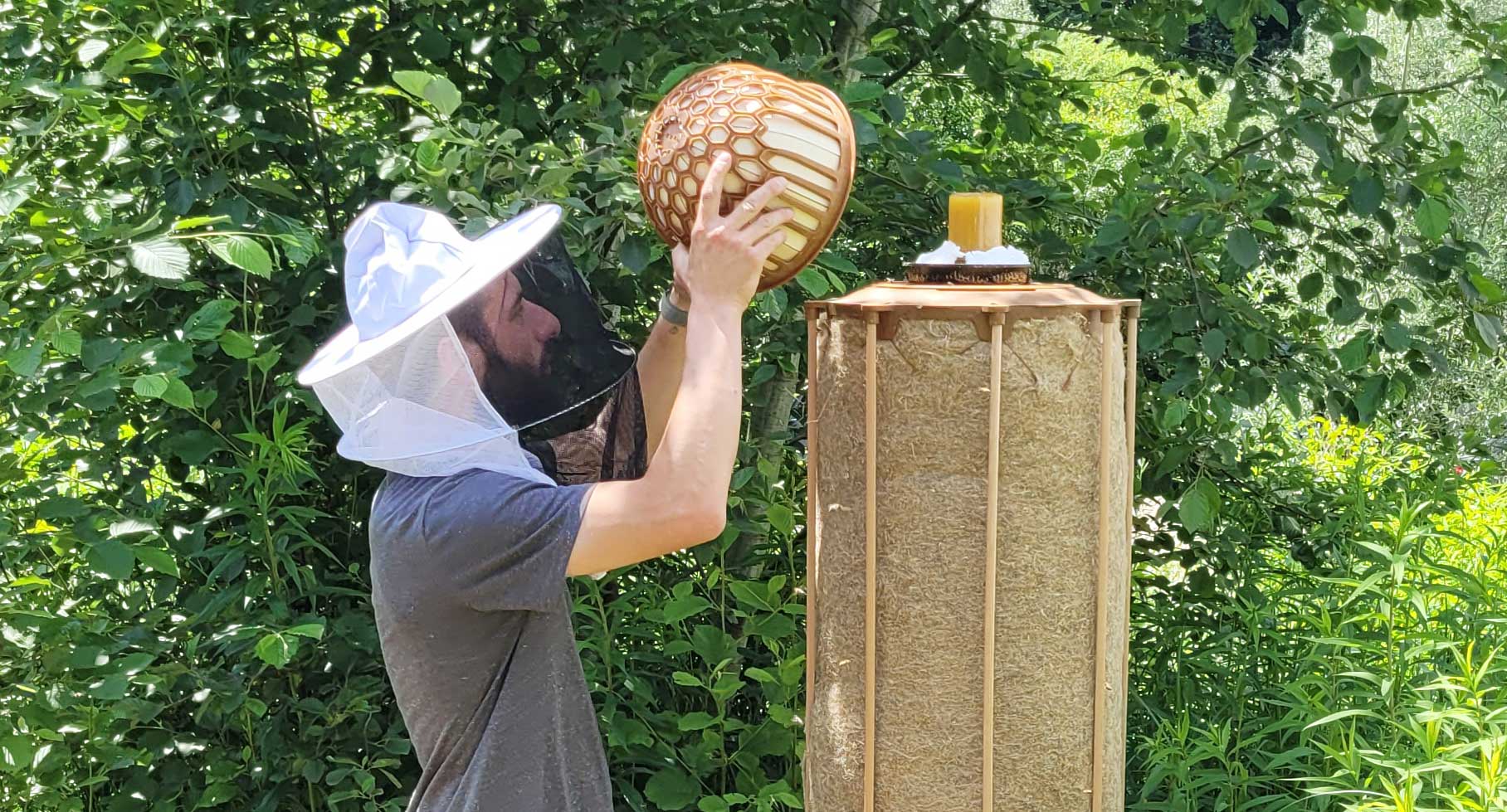 Mann mit Bienenhut neben Bienenstock